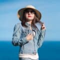Portrait of female in denim jacket, jeans, straw hat and sunglasses on background of blue sky, ocean Portrait of female in denim jacket, jeans, straw hat and sunglasses on background of blue sky, ocean