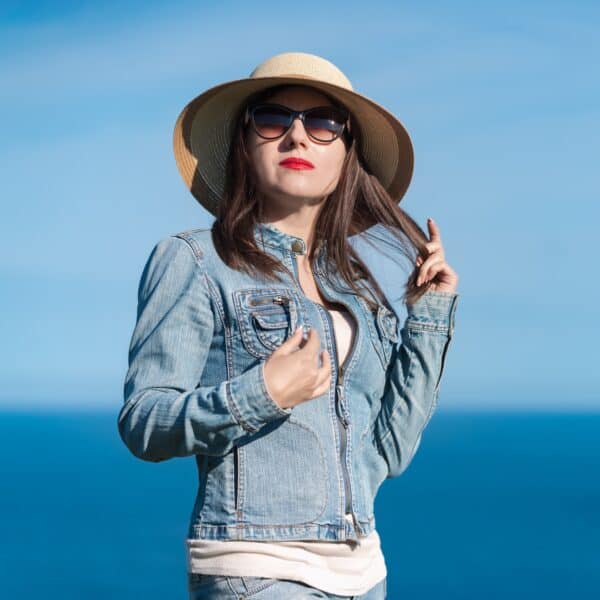 Portrait of female in denim jacket, jeans, straw hat and sunglasses on background of blue sky, ocean Portrait of female in denim jacket, jeans, straw hat and sunglasses on background of blue sky, ocean